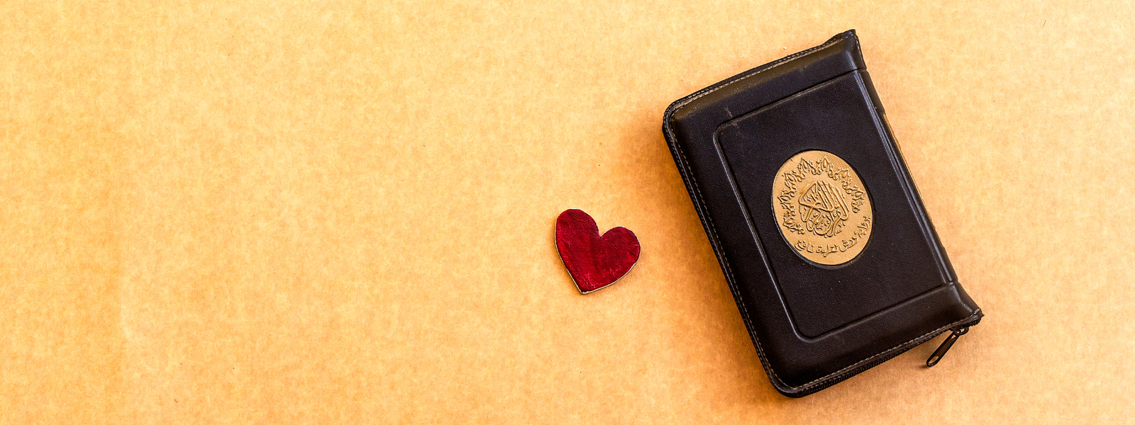 Black leather-bound book with a gold emblem and a red heart on a beige background